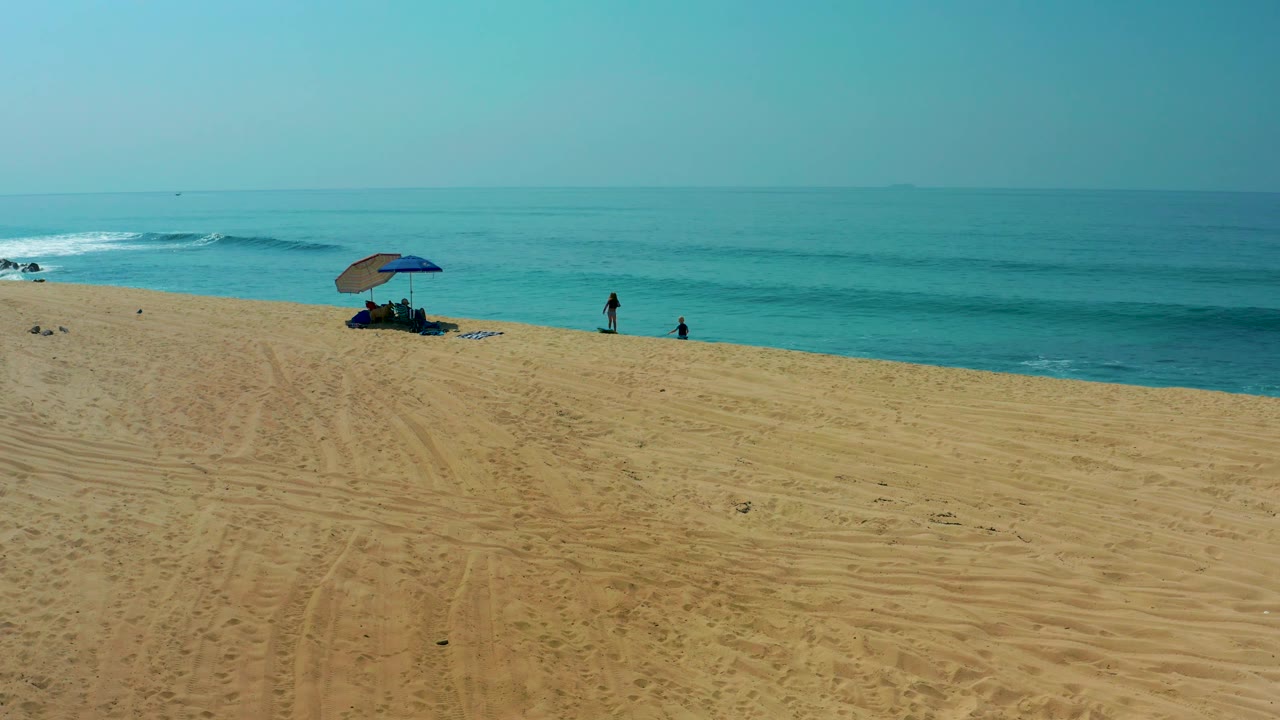 Beach umbrella on open sand with people near rolling ocean waves.