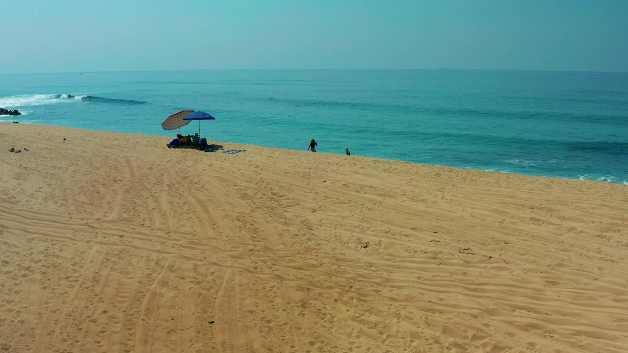 Wide sandy shore with umbrella and ocean waves under blue sky.