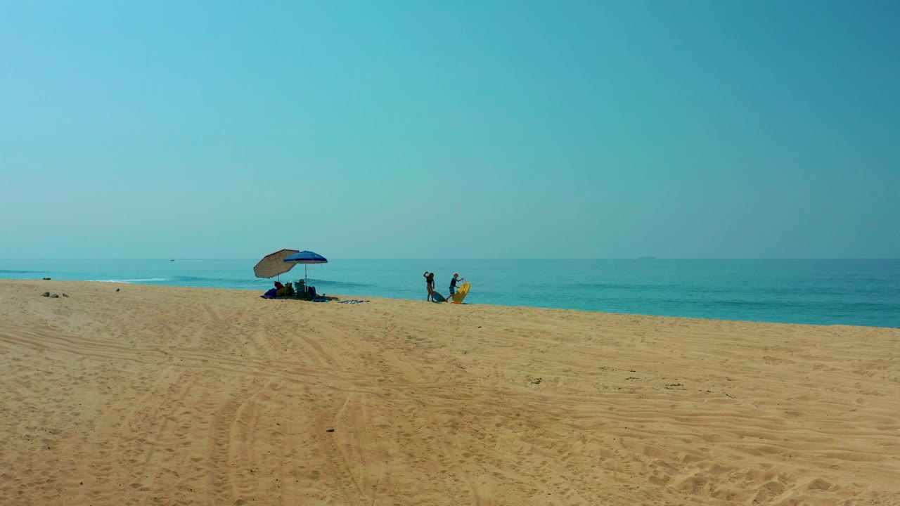 At Shipwrecks Los Cabos, a wide sandy beach stretches toward a blue umbrella beside the ocean while small beachgoers stand and move near the waterline.