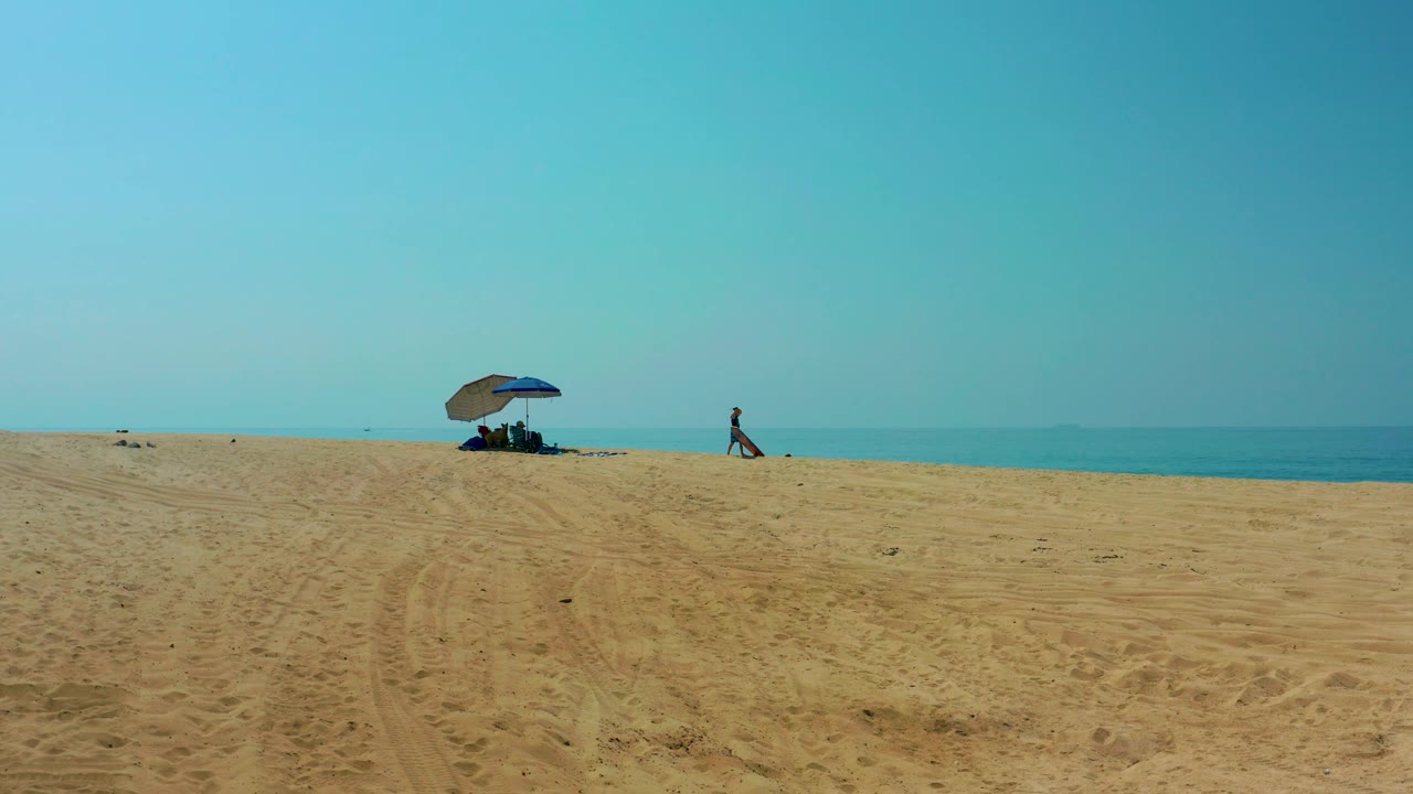 Sandy shore with umbrella group and a person walking near the water.