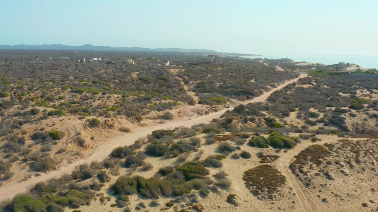 Aerial view of sandy dunes and shrubs with dirt roads leading toward the ocean.