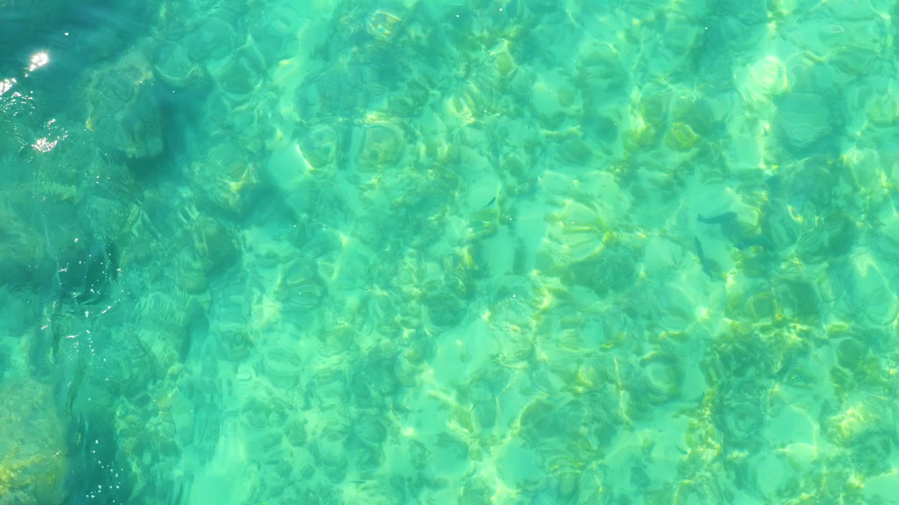 At Shipwrecks Los Cabos, clear turquoise shallow water fills the frame with bright surface ripples over the visible bottom and no visible people.