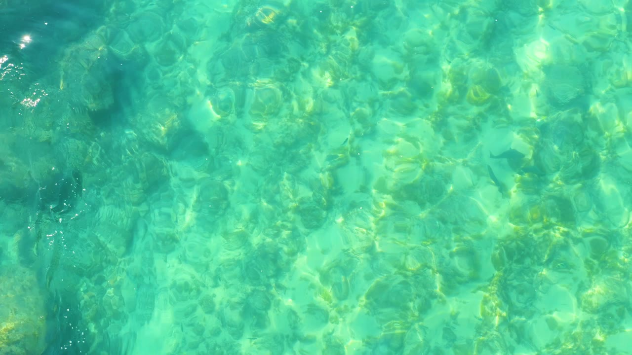 At Shipwrecks Los Cabos, blue-green shallow water shows darker underwater patches, wavering reflected sunlight, and no visible people.