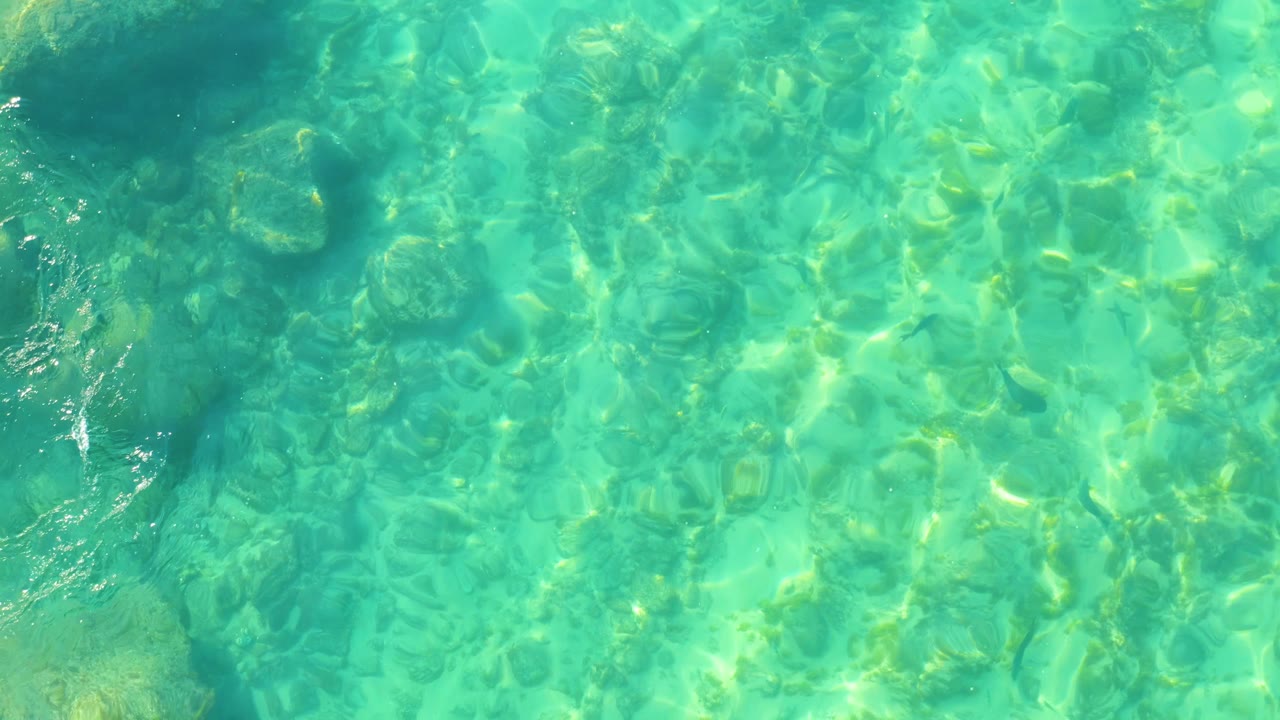 Blue-green shallow water at Shipwrecks Los Cabos shows rippled sunlight crossing uneven submerged rocks, with no visible people.