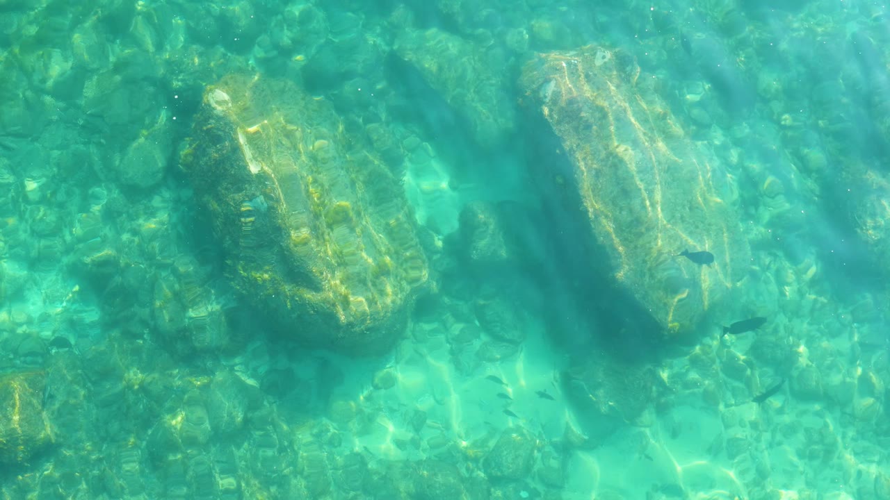 Turquoise shallow water over a rocky seabed at Shipwrecks Los Cabos, with sunlight on pale stones and no visible people.
