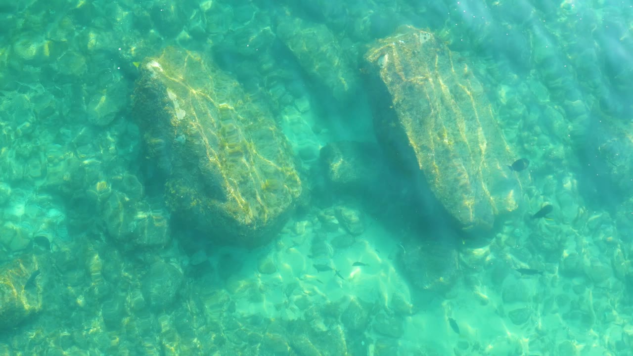 A large pale rock sits near the upper frame under clear water, with turquoise shallows and no visible people at Shipwrecks Los Cabos.