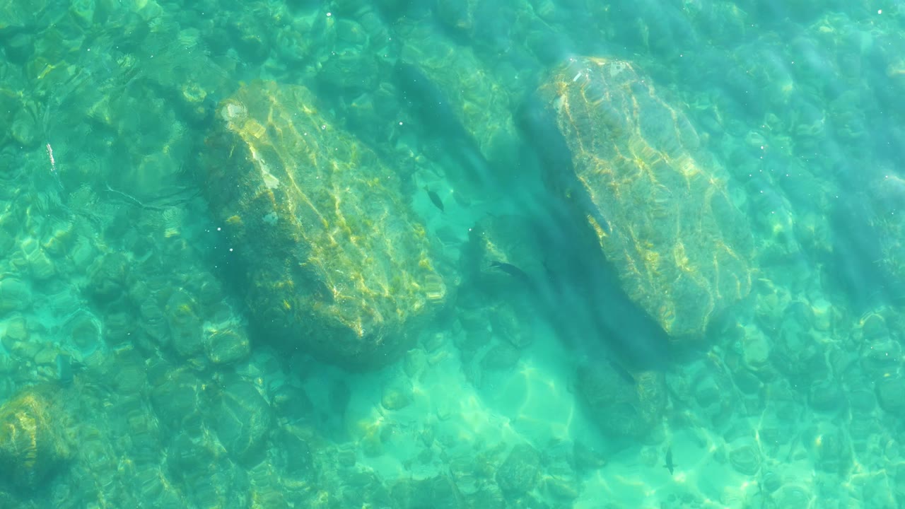 Ripples and caustic sunlight cross a rocky seabed in shallow turquoise water at Shipwrecks Los Cabos, with no visible people.
