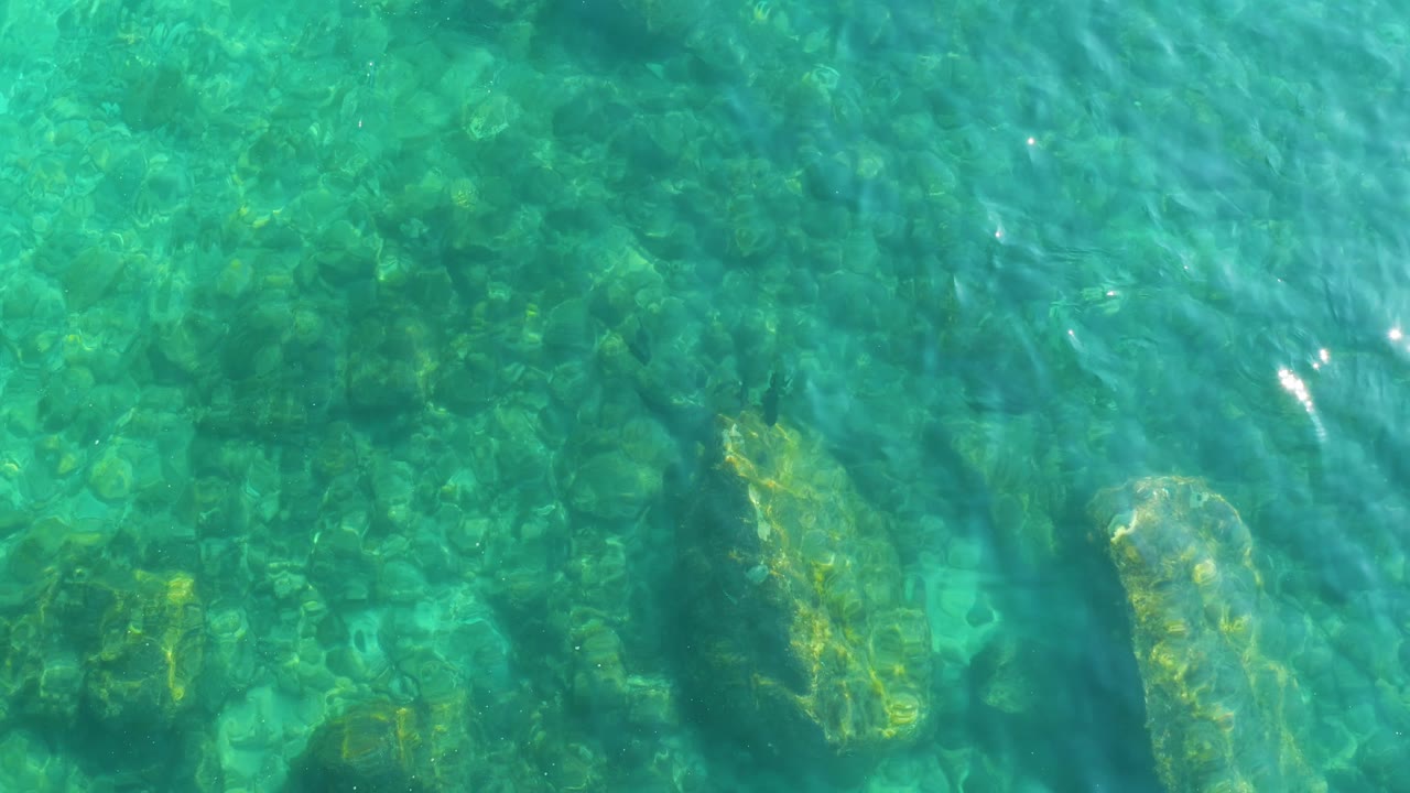 Clear water at Shipwrecks Los Cabos, Baja California Sur reveals rounded underwater rocks and a larger pale rock near the lower right, with no visible people.
