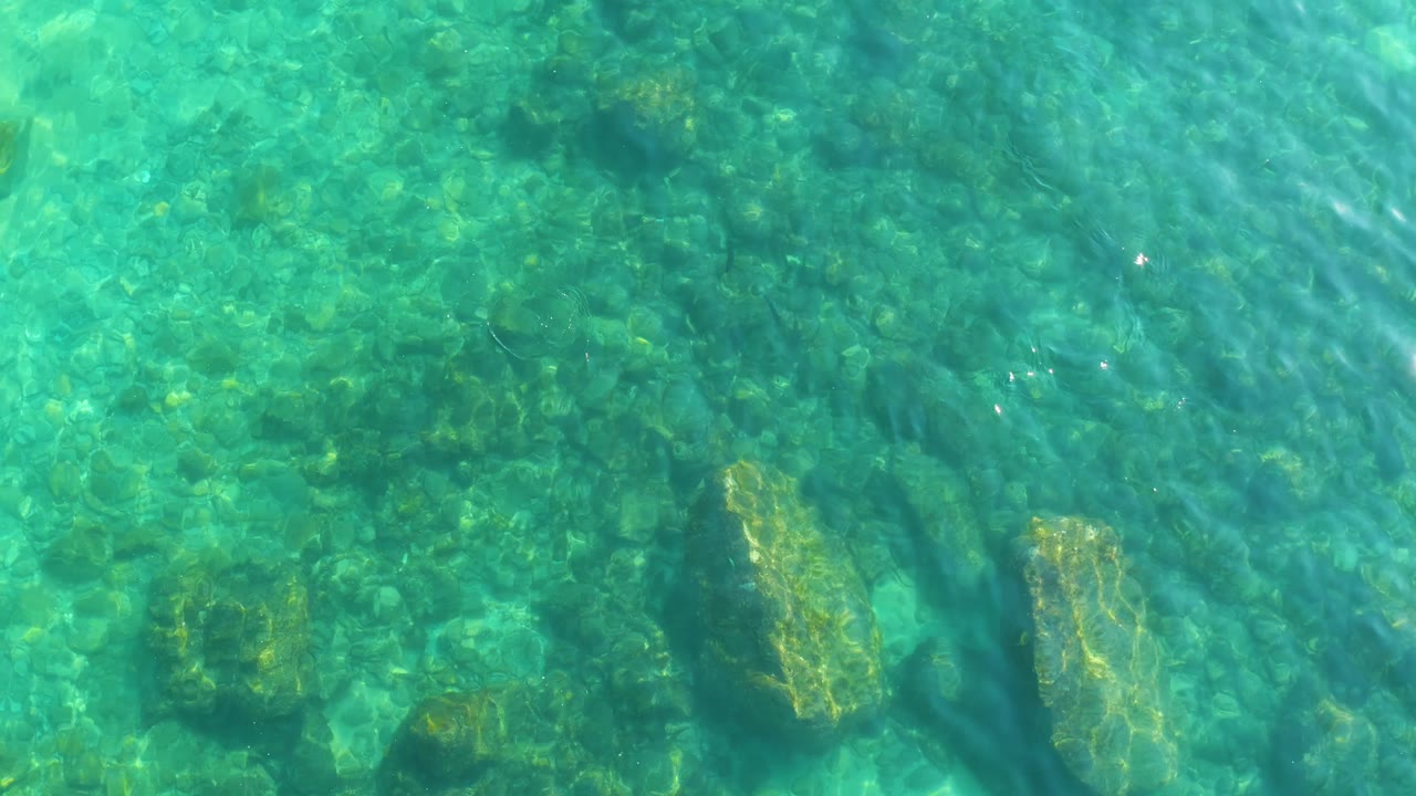Clear turquoise water at Shipwrecks Los Cabos with large submerged rocks, small stones, and wavering light across the seabed, no visible people.
