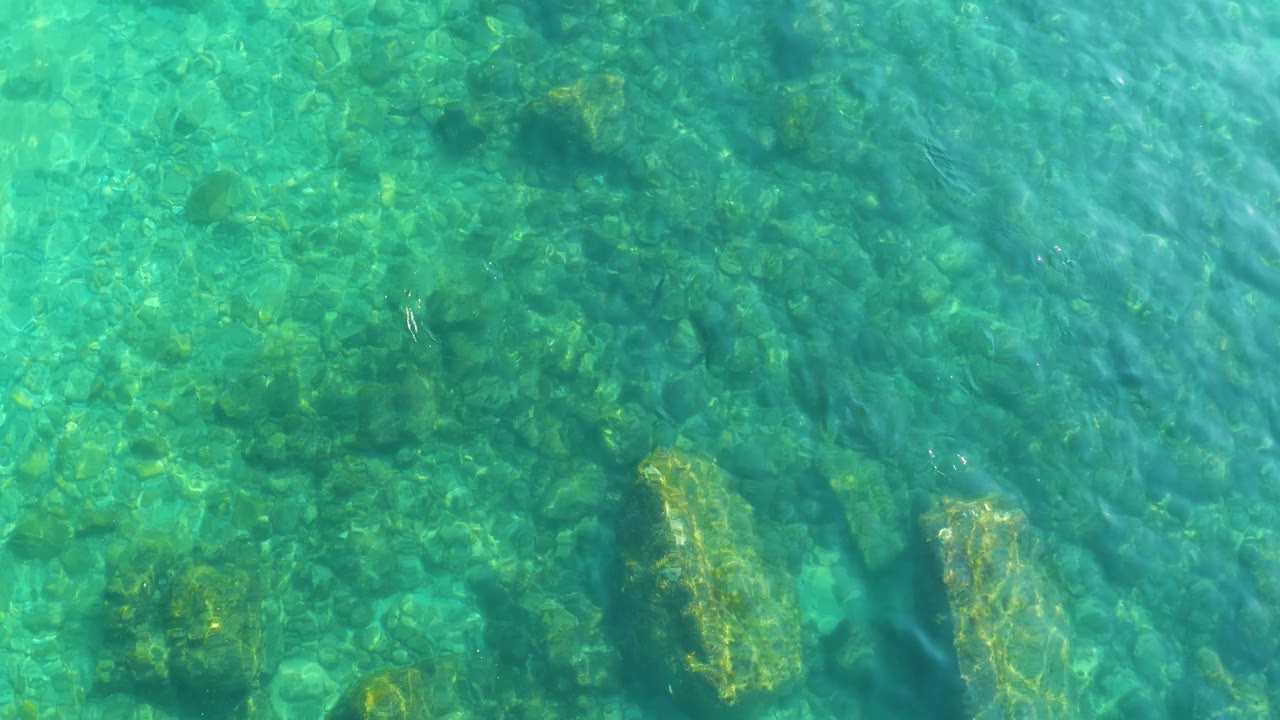 Bright turquoise water at Shipwrecks Los Cabos reveals clustered rocks and darker algae on the ocean floor, with no visible people in frame.