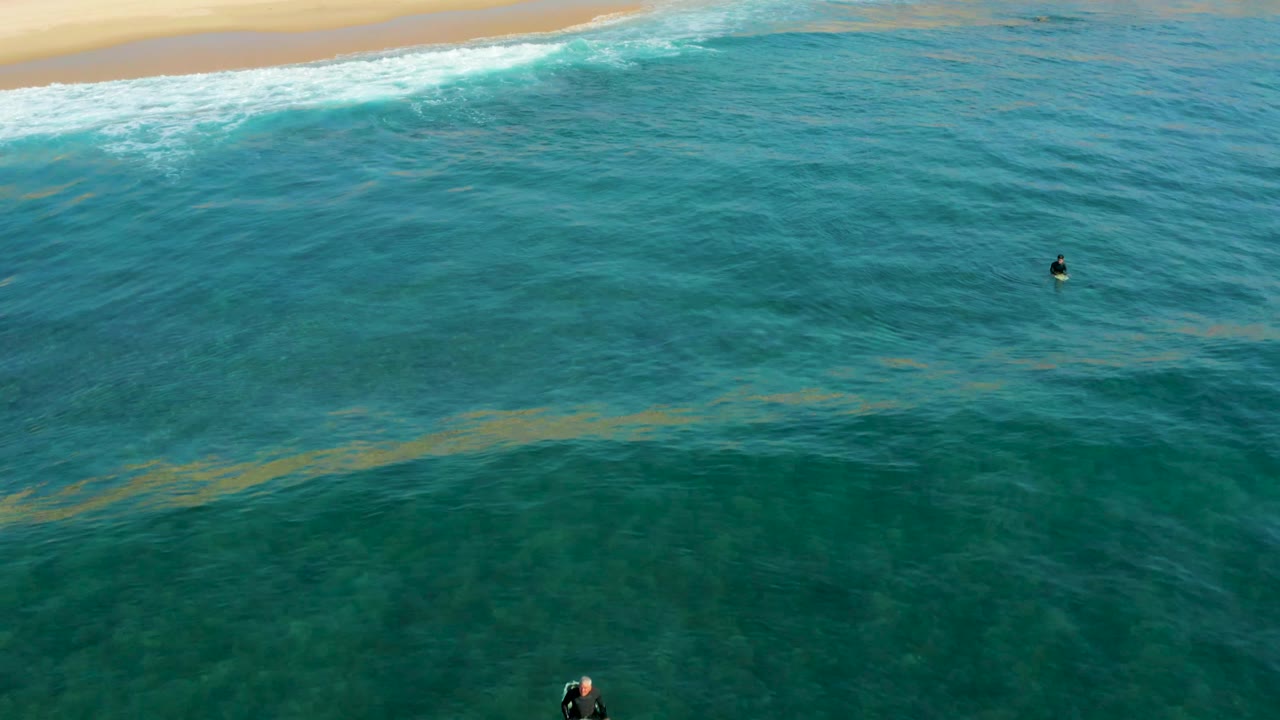 Turquoise ocean and sandy shoreline with two small swimmers in the water.