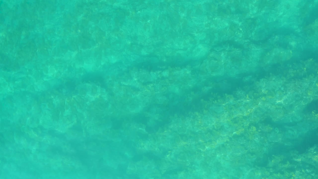 Clear shallow ocean water reveals darker and lighter seabed patches at Shipwrecks Los Cabos, Mexico, with no visible people or vessels.
