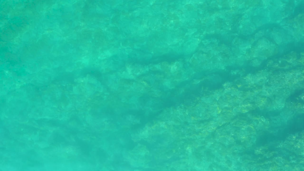 Rippling turquoise water at Shipwrecks Los Cabos passes over shallow rocks, with the seabed softened by the moving surface and no visible people.
