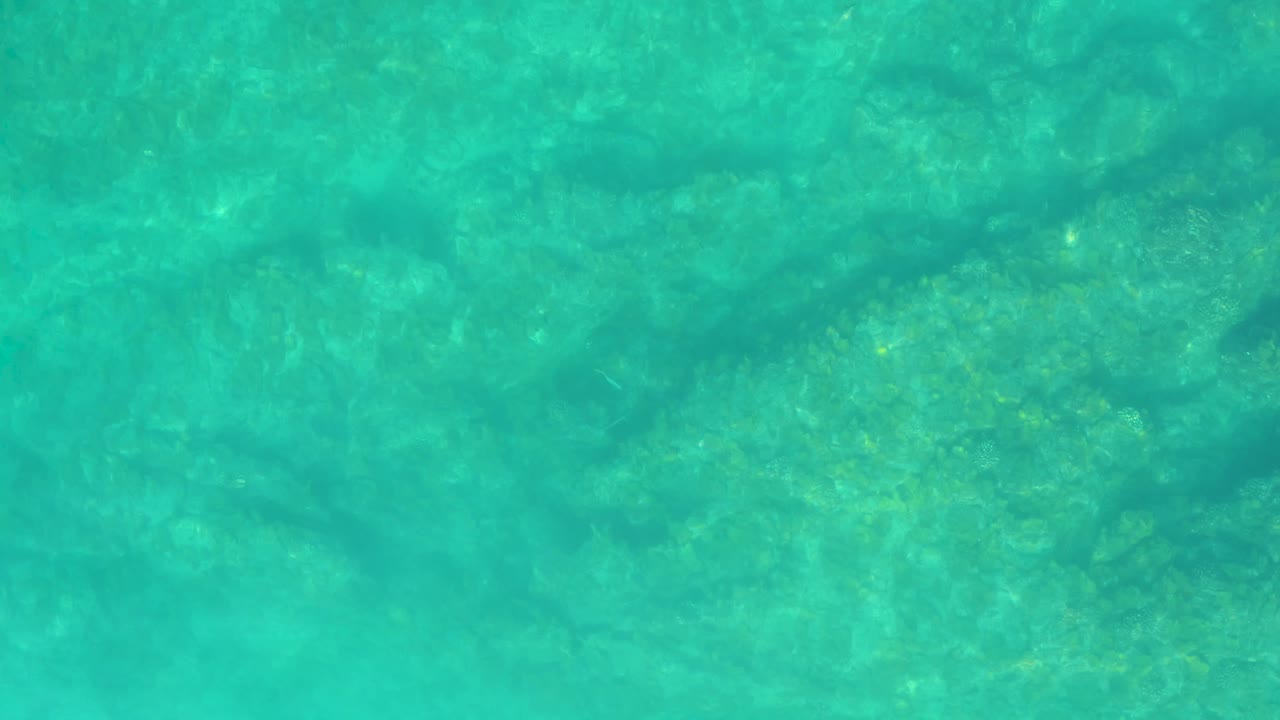 Transparent turquoise water at Shipwrecks Los Cabos fills the frame, with faint wave bands crossing a shallow bottom and no visible people.
