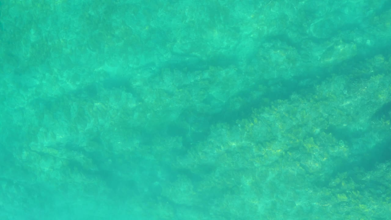 Shallow turquoise ocean water at Shipwrecks Los Cabos reveals mottled rocks or sand below the surface, with gentle ripples and no visible people.