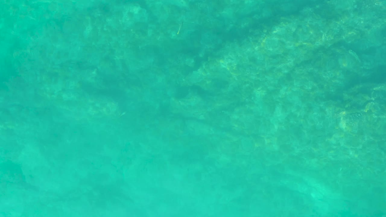 Shallow green-blue water reveals the rocky bottom and a faint small fish shape passing through the frame, with no visible people.
