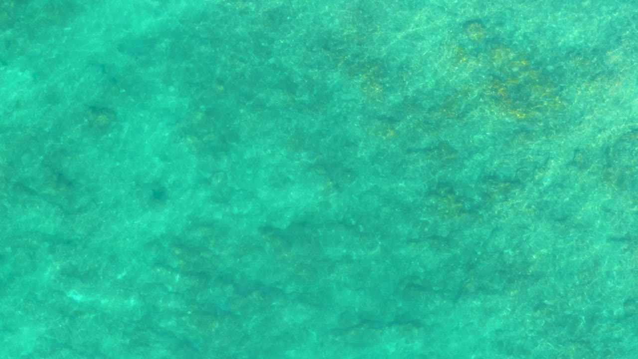Clear blue-green water fills the frame at Shipwrecks Los Cabos, with fine surface ripples slightly shifting the seabed pattern and no visible people.