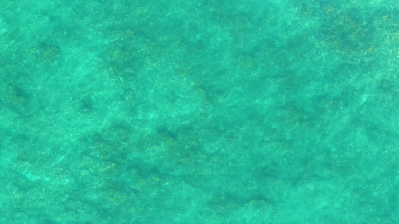 Transparent ocean water at Shipwrecks Los Cabos reveals faint rocky or sandy seabed patterns under green-blue ripples, with no visible people or objects.