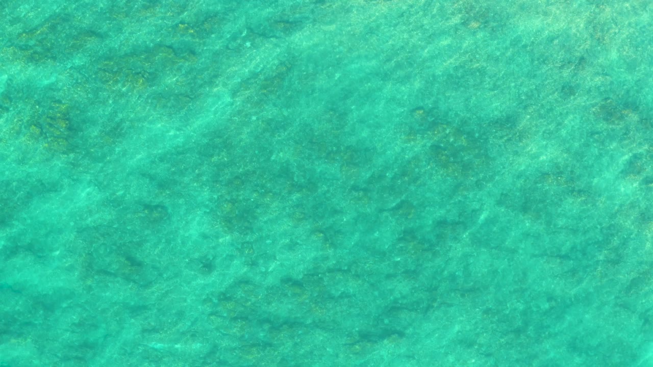 Clear turquoise ocean at Shipwrecks Los Cabos shows darker seabed patches beneath a lightly rippled surface, with no visible people or vessels.