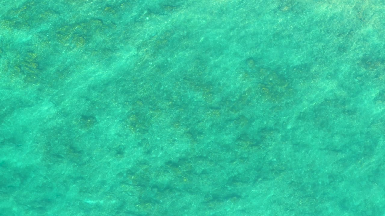 Blue-green shallow water fills the frame at Shipwrecks Los Cabos, with rippled light patterns and mottled seabed detail visible below, and no visible people.
