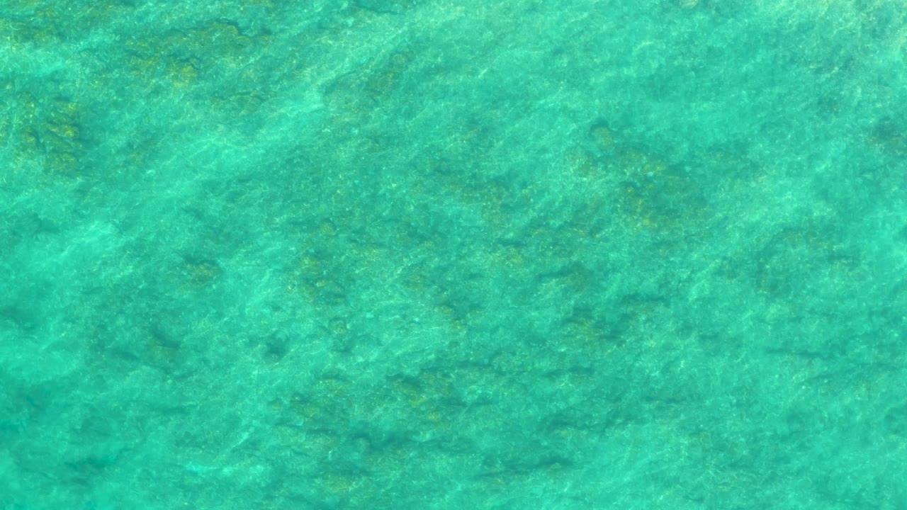 Transparent turquoise water over a mottled shallow seabed at Shipwrecks Los Cabos shows a slightly brighter surface band, with no visible people, boats, or shoreline.