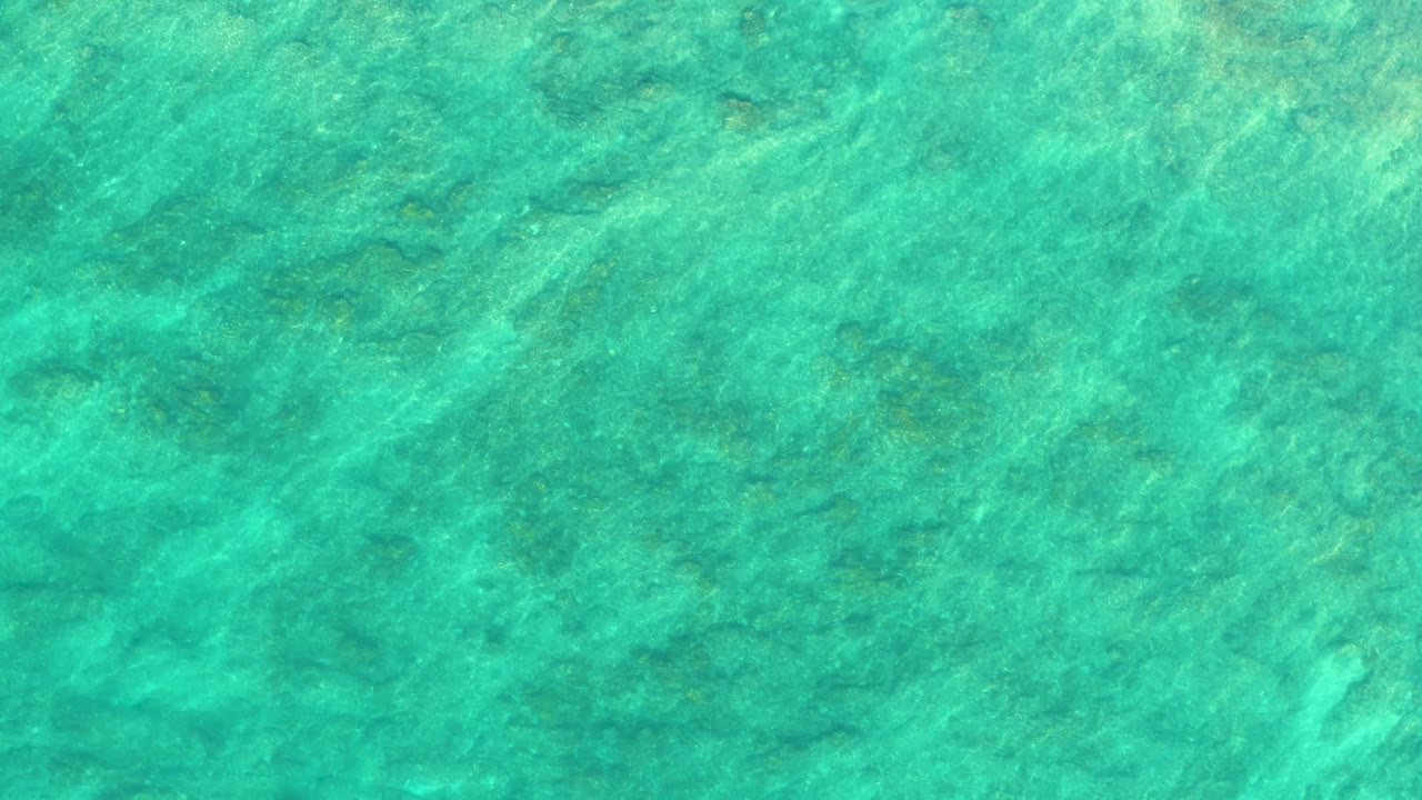 Mid-clip overhead view of Shipwrecks Los Cabos water, showing ripples and green-blue color over a textured seabed with no visible people or vessels.