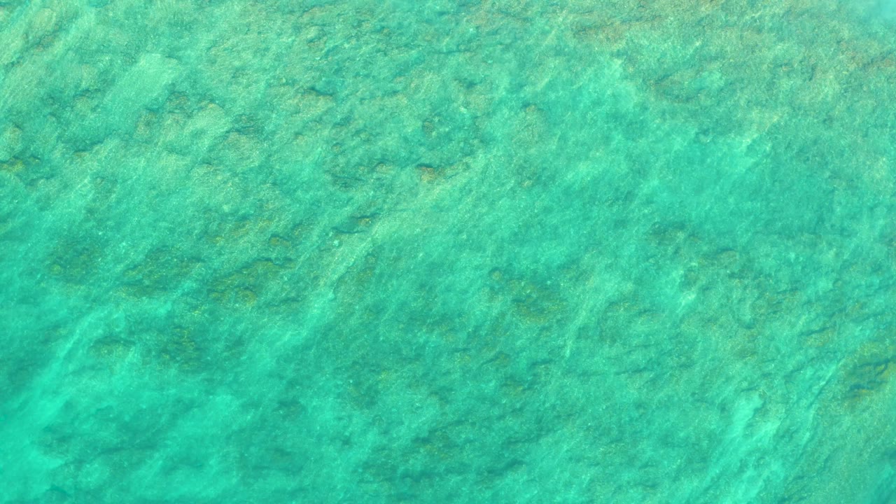 Opening frame of turquoise shallow water over the seabed at Shipwrecks Los Cabos, with faint ripples and no visible people.