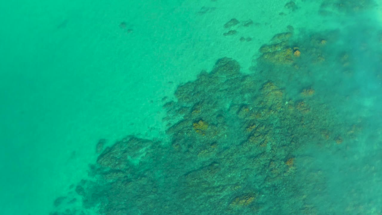 Shallow turquoise sea over a broad reef structure at Shipwrecks Los Cabos, with darker texture lower right and no visible people.