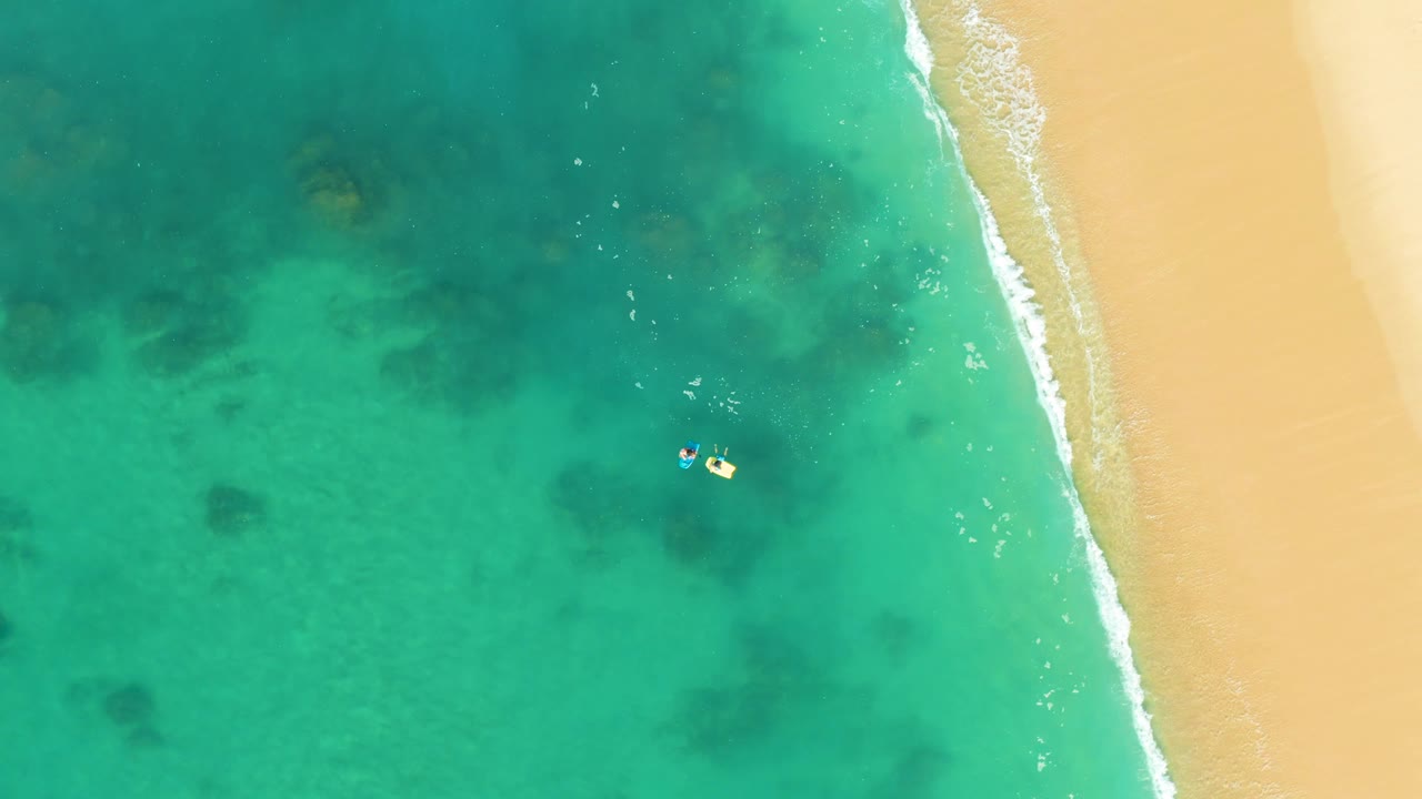 Clear ocean water with two swimmers floating near the surf line.