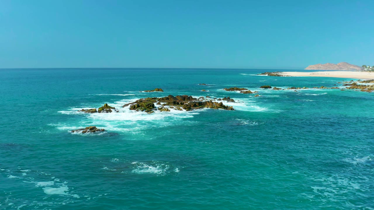 Turquoise ocean waves breaking around dark shoreline rocks