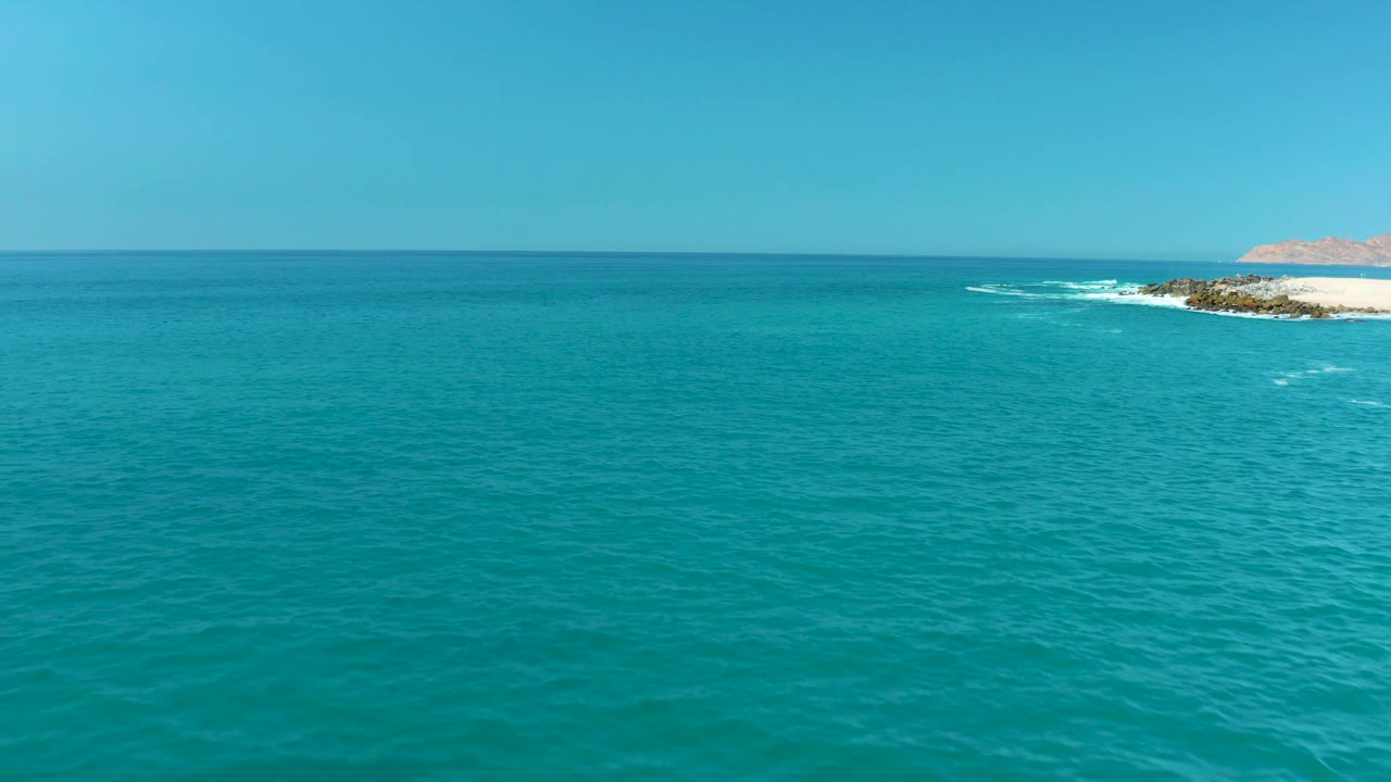 Calm turquoise ocean below a clear horizon with rocks and surf at right.