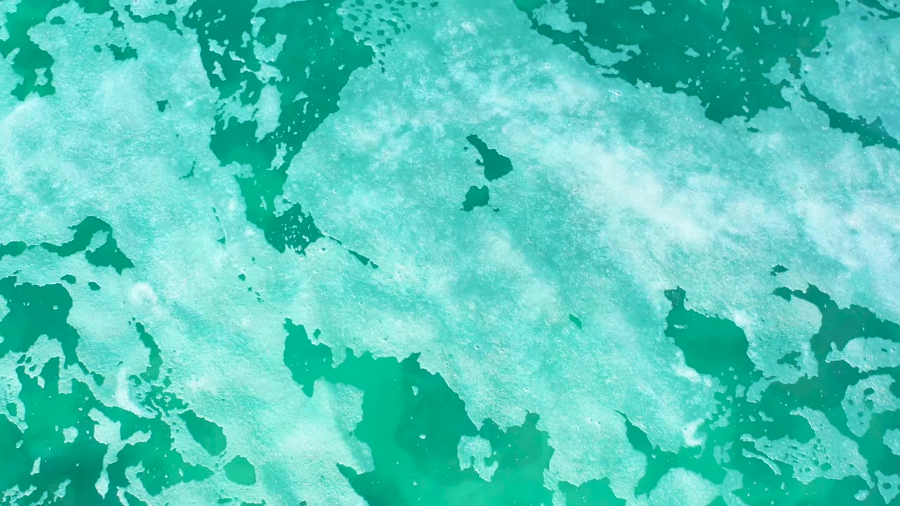 At 0:03, blue-green ocean water fills the frame while white foam patches form a loose diagonal texture, and no visible people appear.