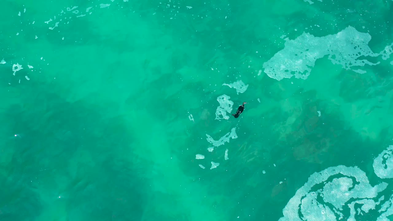 Small swimmer crossing turquoise water near foamy white patches.