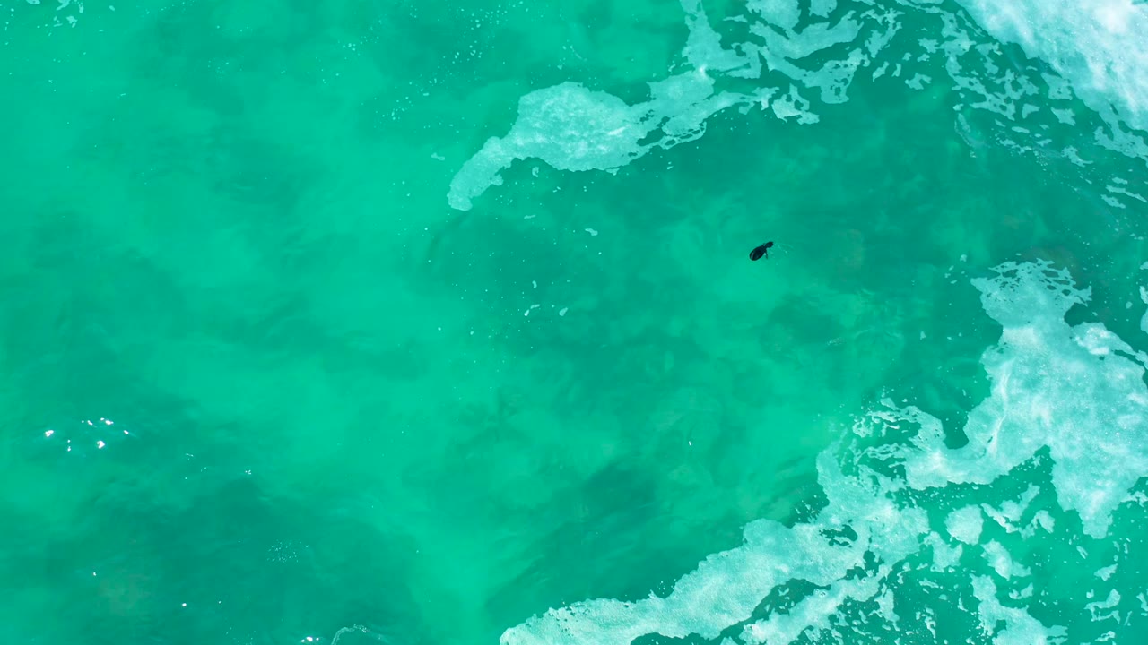 Clear green-blue ocean water with foam bands and a small swimmer.