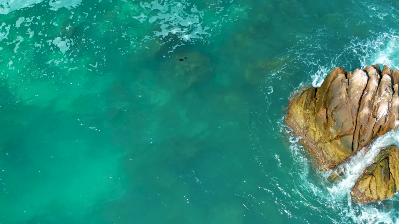 Aerial view of rocks surrounded by turquoise water and foam.