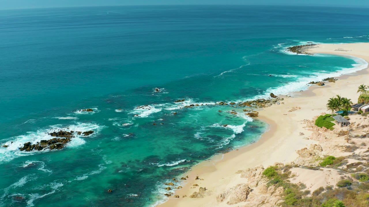 Marquis Los Cabos, Mexico aerial still with more open blue water filling the left side, reef rocks below, a pale sandy beach on the right, and no visible people.