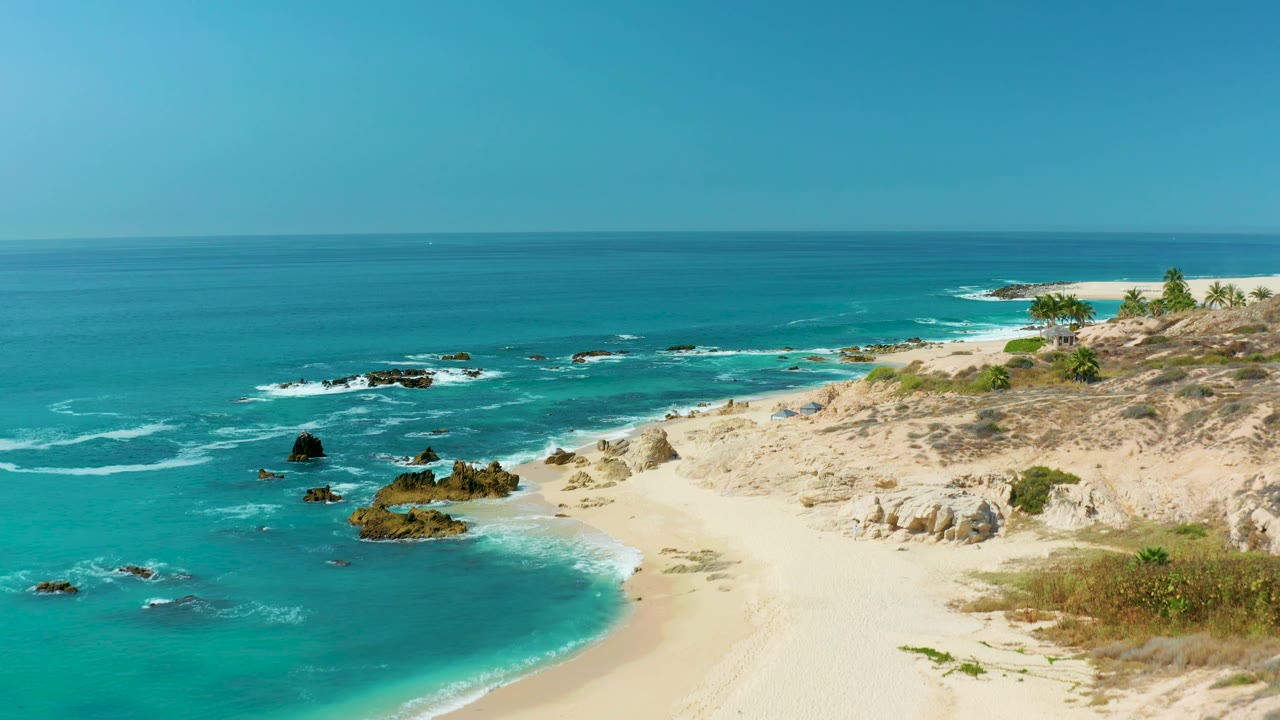 Elevated coastal view at Marquis Los Cabos, Mexico, with surf tracing around dark rock outcrops and a pale sand cove, no visible people.