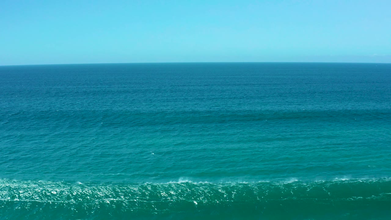 Turquoise ocean with a breaking wave line and blue horizon.