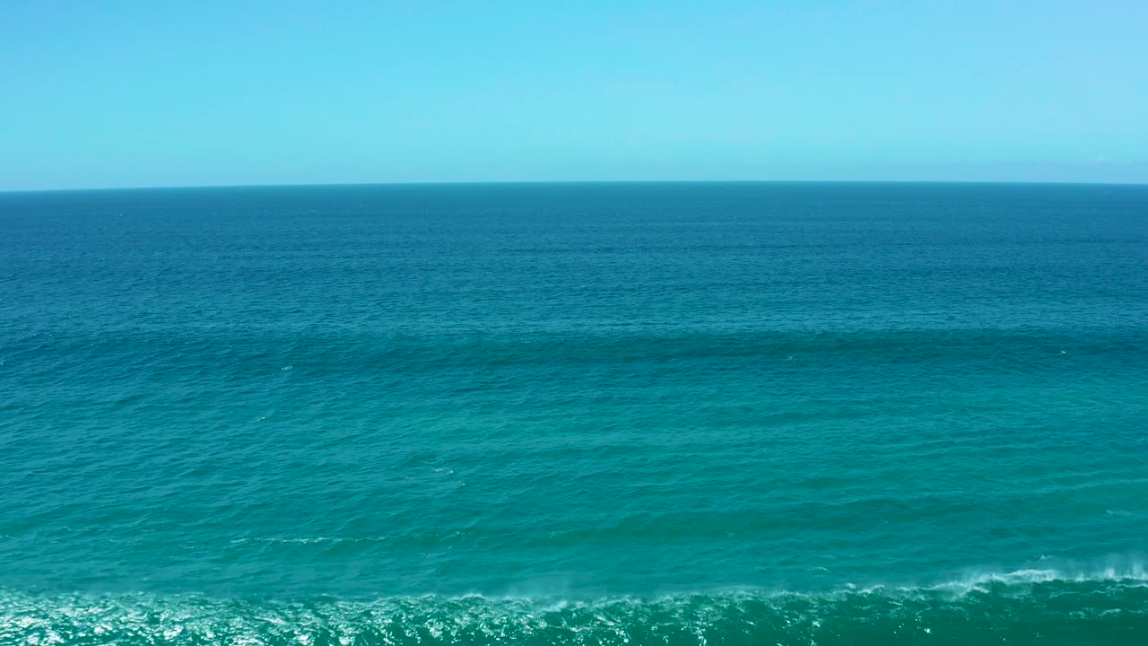 La Laguna Beach Los Cabos ocean surface fills the frame with blue green water, a level horizon, and only a small trace of foam at the lower edge, no visible people.