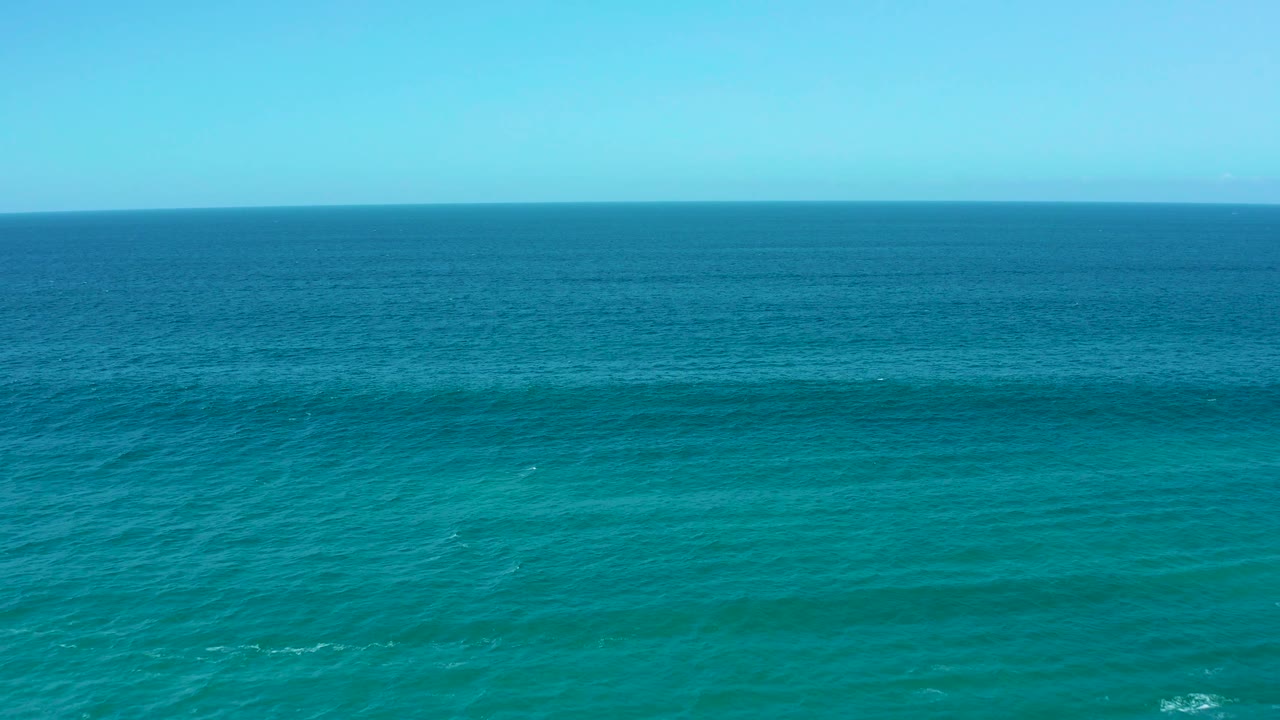 Wide aerial view at La Laguna Beach Los Cabos showing turquoise foreground water, darker offshore water, and an uncluttered horizon, no visible people.