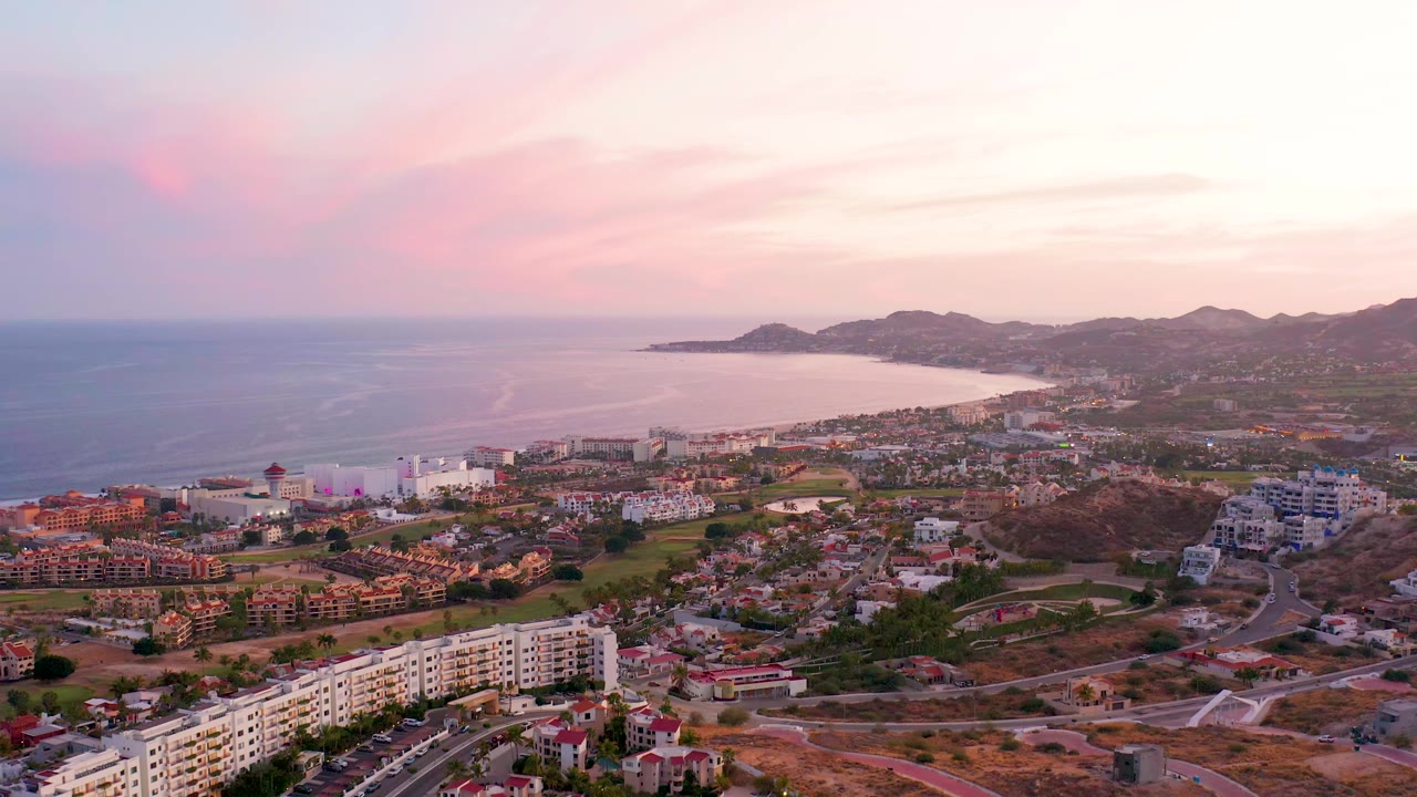 Coastal aerial with ocean, curved shoreline, town buildings, and pink sky
