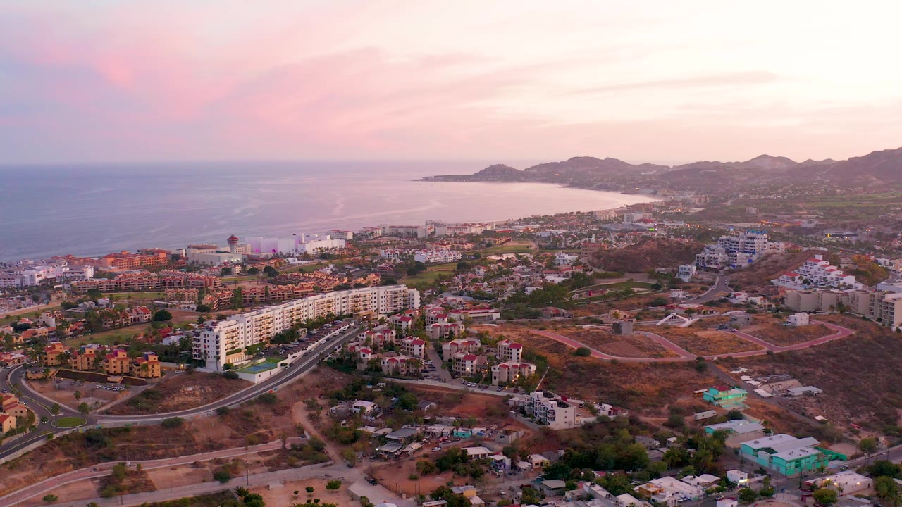 Aerial townscape with ocean bay, hillside, roads, and pink clouds at dusk.