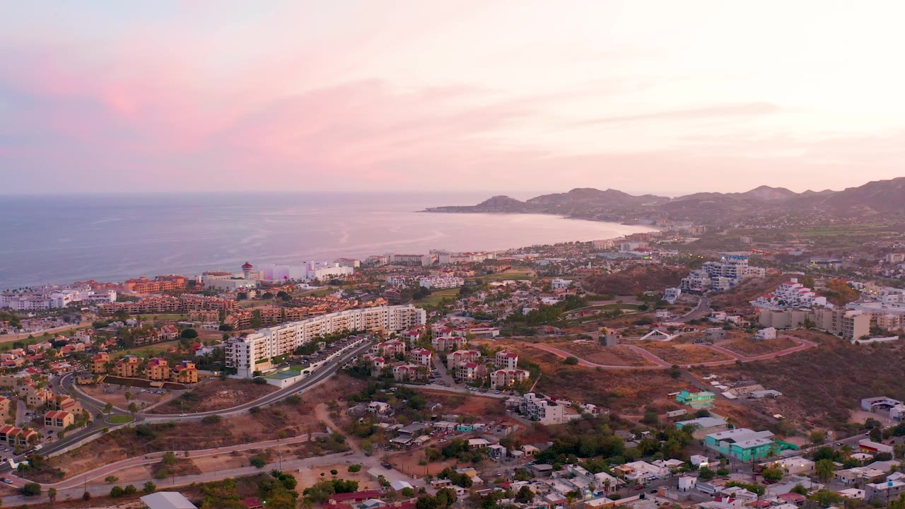 San Jose del Cabo aerial frame with the shoreline stretching across the background, roads and homes below, low mountains beyond the city, and no visible people.