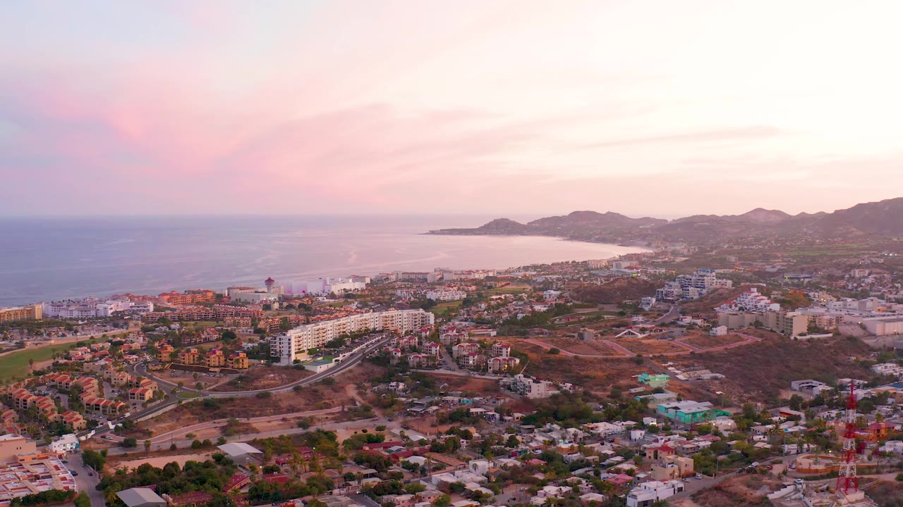 Aerial coastal cityscape with buildings, roads, ocean, and pastel sky.