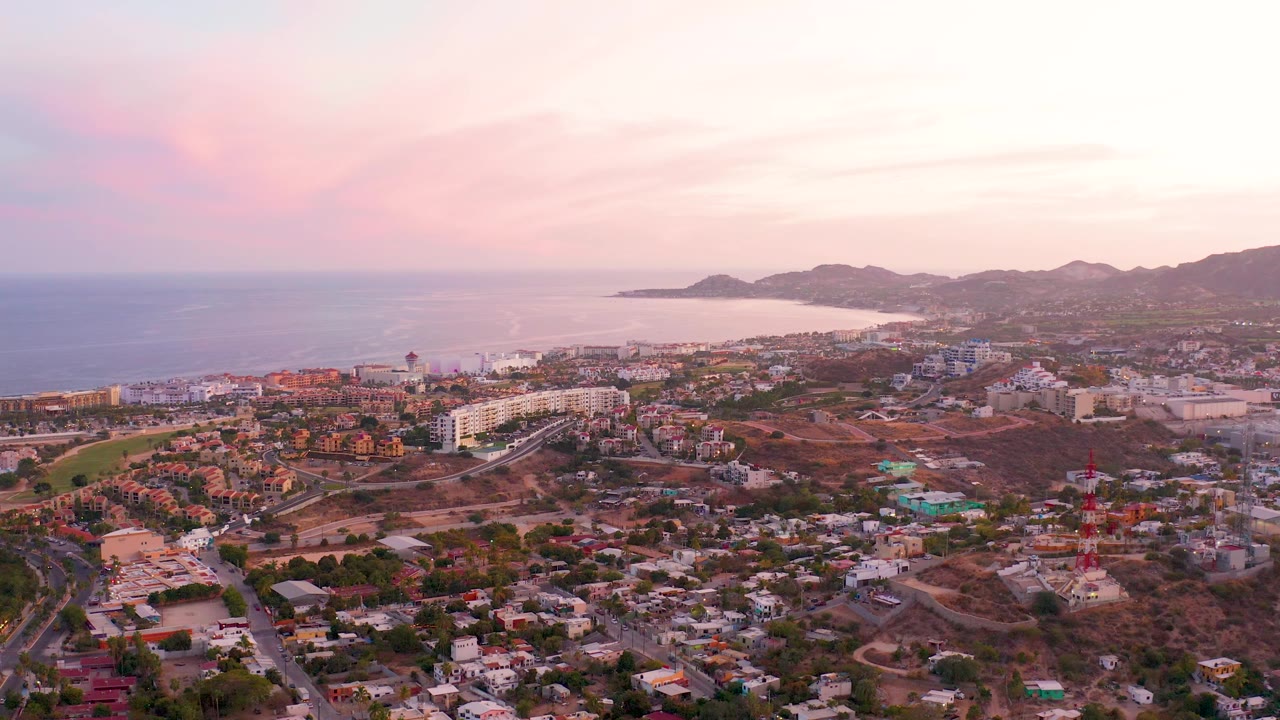 Aerial frame of San Jose del Cabo with the coastline stretching across the left background, hills along the horizon, compact residential areas below, and no visible people.
