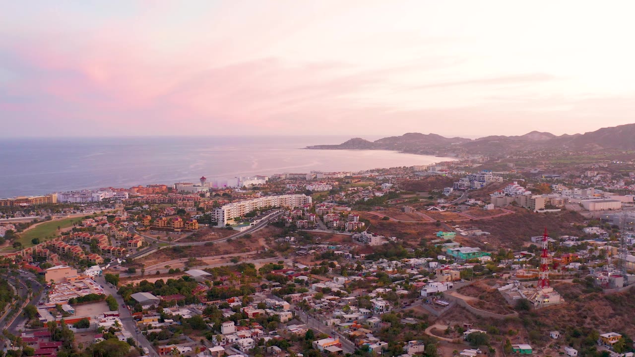 Aerial coastal town view with roads, buildings, hills, and dusk sky.