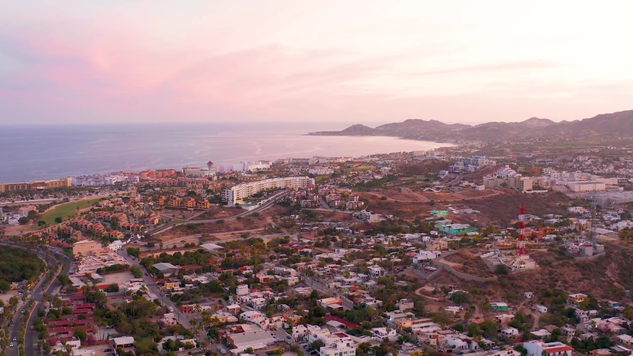 Aerial coastal city view with roads, hills, and ocean horizon.