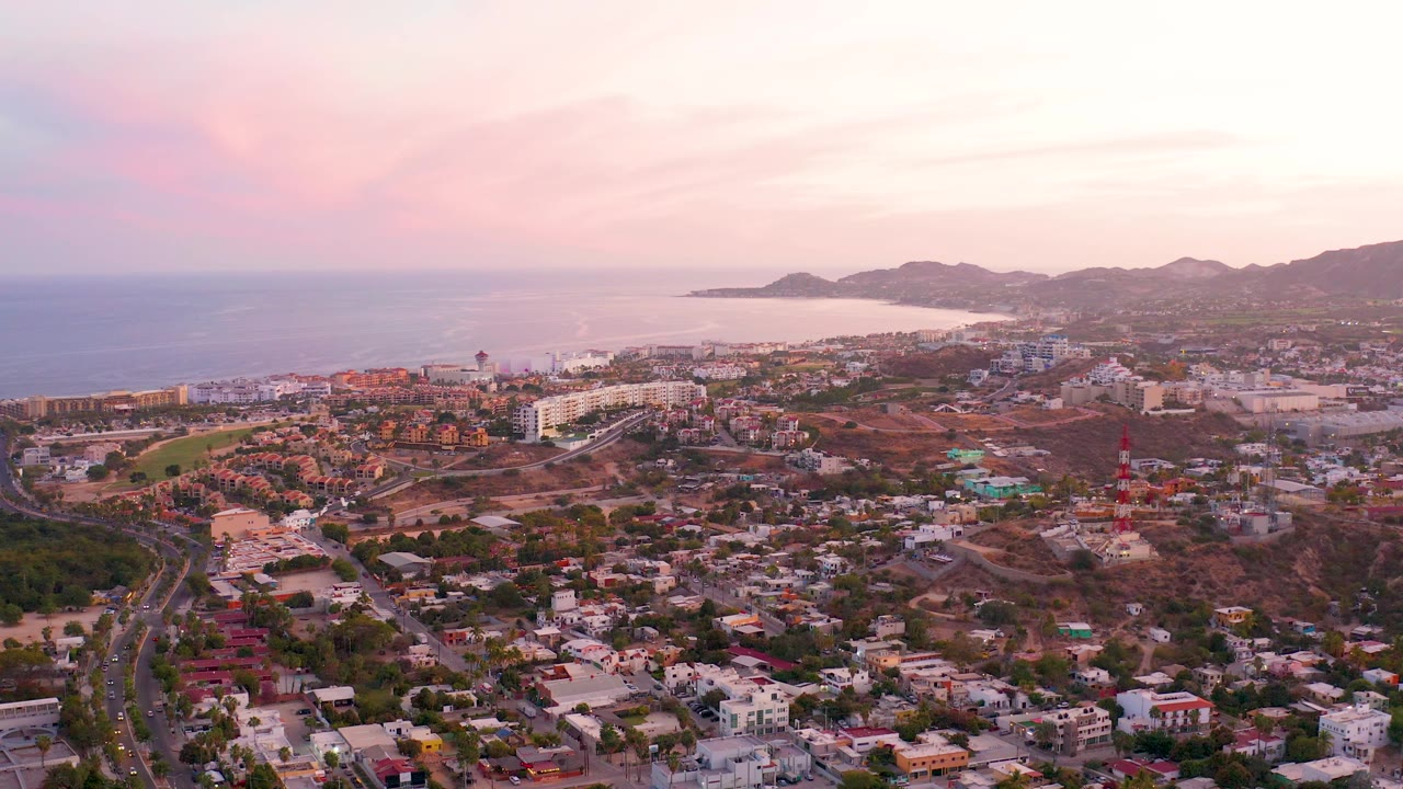 Elevated view of homes, curving road, ocean horizon, and dusk clouds.