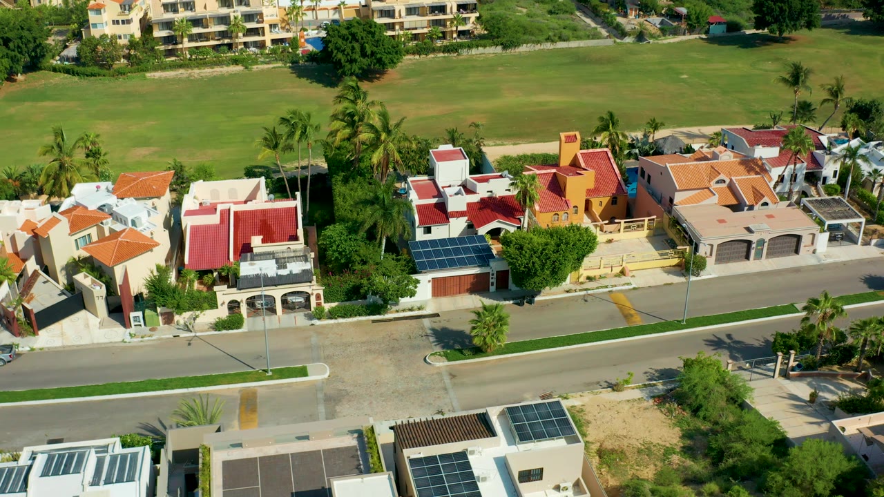 Aerial view in San Jose Del Cabo with the road running across the middle, colorful house roofs below the green field, palm trees near the homes, and no visible people.