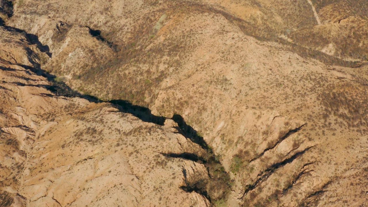 Overhead frame from Cabo Pulmo, Baja California Sur, Mexico, showing tan rocky ridges, sparse scrub, and a dark winding river channel with no visible people.